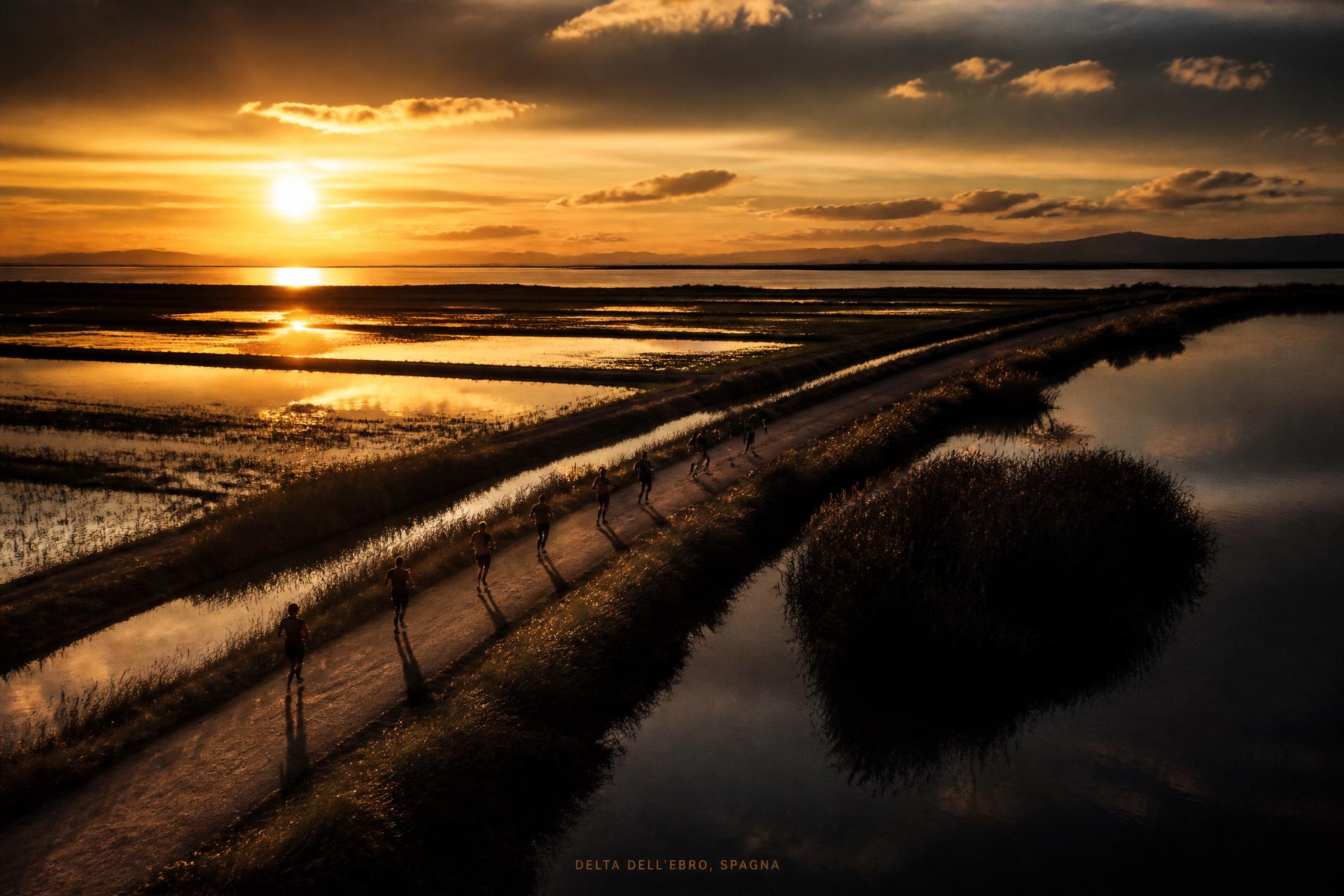 Atardecer en el Delta de l'Ebre con atletas corriendo por un camino entre arrozales